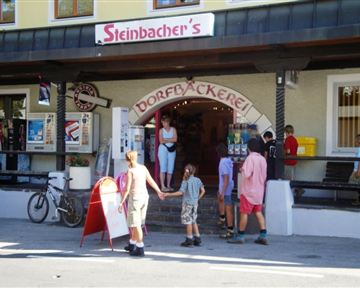 A traditional village bakery with an entrance that attracts guests. Children are standing nearby, waiting for their treats.