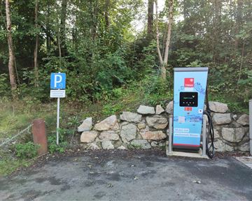 Eine Ladestation für Elektroautos in einer waldreichen Umgebung. Neben der Station steht ein Parkplatzschild.