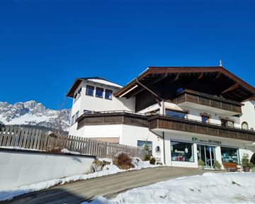 Ein charmantes alpenländisches Haus mit mehreren Etagen. Der Himmel ist klar und blau, und es liegt Schnee auf dem Boden.