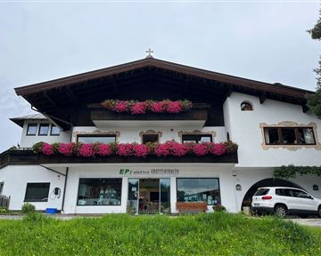 Ein charmantes Haus mit traditoneller Architektur, geschmückt mit bunten Blumen. Im Vordergrund parkt ein Auto, umgeben von einer grünen Wiese.