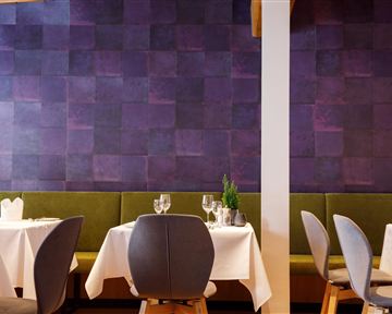 Ein stilvolles Restaurant mit eleganten Tischen und modernen Stühlen. Die Wände sind in einem schönen lila Farbton gestaltet.