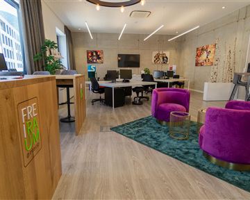 A modern office with bright colors and stylish furniture. In the foreground, there are two purple armchairs on a carpet.