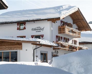 A cozy chalet in the snow with balconies and traditional windows. The surroundings are covered by a deep layer of snow.
