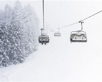 Eine schneebedeckte Landschaft mit einem Skilift in der Mitte. Die Bäume im Hintergrund sind von Schnee umgeben und die Sicht ist eingeschränkt.