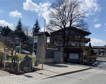 A charming building on a quiet street, surrounded by trees and beautiful countryside. The sky is clear with some clouds.