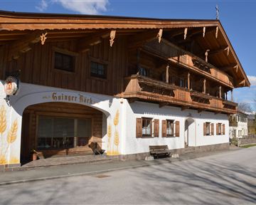 A traditional Bavarian guesthouse with a wooden-paneled facade. It has large balconies and appears to be situated in a quiet rural setting.