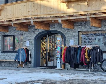 A sporting goods store with an inviting entrance. Various clothing items hang on racks in front of the store.