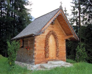A small wooden church stands amidst trees. Surrounded by green grass, it appears peaceful and inviting.
