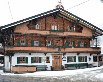 A traditional wooden house in Bavarian style, surrounded by snow. The green shutters and balconies give the building a charming look.