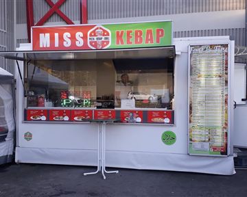 A kebab stand named "Miss Kebap" with a large menu at the front. The stand is clean and well-lit, ideal for outdoor snacks.
