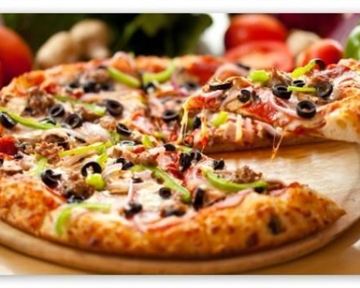 A delicious pizza with cheese, meat, olives, and bell peppers. Fresh vegetable ingredients can be seen in the background.