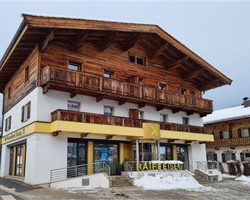 A traditional wooden house with several balconies in the Alps. Below is a shop with a yellow sign.