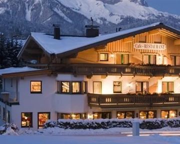 A cozy hotel in the snow with illuminated windows. In the background, snow-covered mountains and trees can be seen.