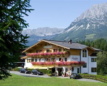 A charming chalet in the mountains with colorful flowers on the balconies. In the background, majestic mountains stretch under a blue sky.
