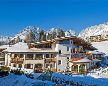 A cozy hotel in a snow-covered landscape. In the background, majestic mountains and a clear blue sky can be seen.