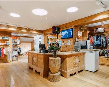 Ein gemütlicher Laden mit Holzdekor und einer Vielzahl von Bekleidungsstücken. An der Kasse steht eine Pflanze in einem dekorativen Topf.