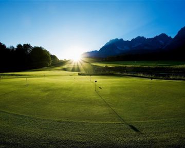 A beautiful golf course landscape at sunrise. The mountains in the background and the green grass create a serene atmosphere.