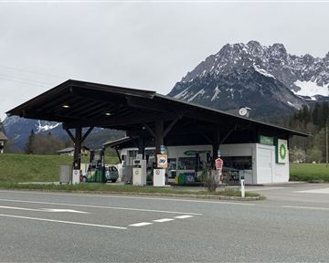 A gas station with a covered area in a rural environment. Impressive mountains can be seen in the background.