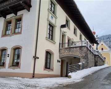 A picturesque building in the mountains, surrounded by snow. The architecture is traditional with wooden embellishments and large windows.