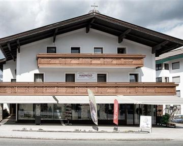 Ein modernes Gebäude im alpinen Stil mit Holzverkleidung und Balkonen. Der Himmel ist bewölkt und es gibt eine ruhige Straße vor dem Haus.
