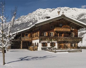 Ein gemütliches Holzhaus im Schnee mit einem malerischen Bergpanorama. Die Landschaft ist ruhig und winterlich, mit schneebedeckten Bäumen.