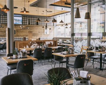 Ein modernes Restaurant mit Holzinterieur und gemütlicher Atmosphäre. Die Tische sind elegant gedeckt und es gibt viele Pflanzen.