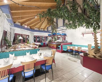 A cozy restaurant with a wooden ceiling and colorful seating. The tables are elegantly set and offer space for many guests.