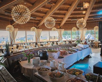 Ein elegantes Restaurant mit Holzdecke und stilvollen Leuchten. Am Buffet stehen verschiedene köstliche Speisen bereit.