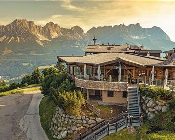 A picturesque building on a hill overlooking majestic mountains. The evening sun bathes the landscape in warm light.