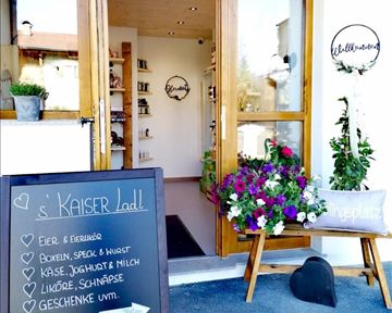An inviting shop entrance with wooden doors and colorful flowers. In the foreground, there is a sign offering fresh produce and gifts.