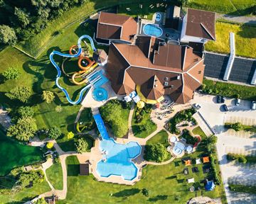A large recreational facility with several swimming pools and slides. The complex is surrounded by green meadows and trees.