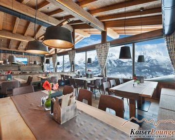 A cozy restaurant with wooden decor and modern lamps. Large windows offer a view of the mountains and let in plenty of daylight.