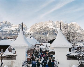 A snow-covered landscape with majestic mountains in the background. Visitors explore the picturesque town under a clear sky.