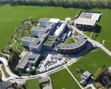 A modern building complex in a green landscape. The structure includes several separate buildings and is surrounded by lawns.