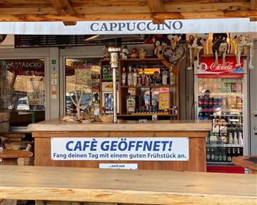 Ein Café mit einer Holzbar und Getränken. Ein Schild besagt, dass das Café geöffnet ist und Frühstück anbietet.