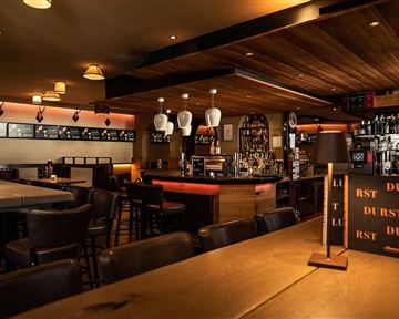 Eine gemütliche Bar mit Holzinterieur und dimmbarer Beleuchtung. Der Thekenbereich ist gut bestückt und einladend.