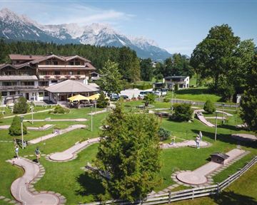 Eine schöne Mini-Golfanlage mit gepflegten Bahnen und viel Grün. Im Hintergrund sind Berge und ein Hotel zu sehen.
