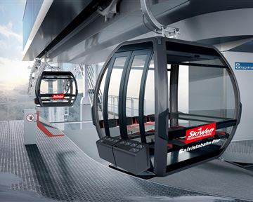 Eine moderne Seilbahnstation mit zwei Gondeln. Die Umgebung zeigt eine alpine Landschaft und ist für den Wintersport geeignet.