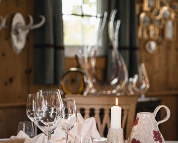 Ein stilvoll gedeckter Tisch mit Gläsern, Servietten und einer Kerze. Im Hintergrund sind Holzverkleidungen und dekorative Elemente zu sehen.