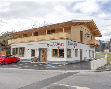 A modern building in alpine style is located at a street corner. A red car is parked in front of the house.
