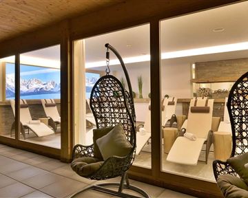 A modern relaxation area with hanging chairs and loungers. Large windows offer a view of the mountains and create a calm atmosphere.