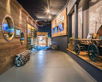 Ein moderner Flur mit Holzwänden und einer attraktiven Ausstellung. An den Wänden sind Bilder und Informationen zu sehen, während die Beleuchtung eine einladende Atmosphäre schafft.