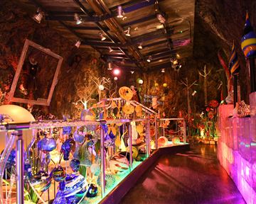 A colorful room with artistic glass sculptures and colored light. The walls are made of rock, creating a unique atmosphere.
