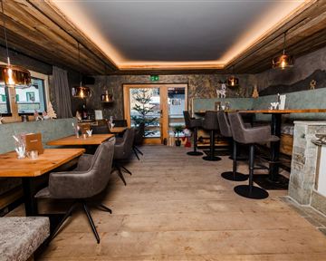 Ein modernes Restaurant mit Holzböden und gemütlichen Sitzplätzen. Große Fenster bieten einen Blick nach draußen auf einen Baum.