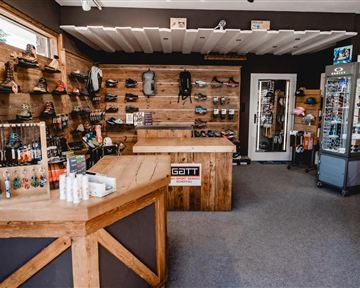 A sporting goods store with wooden shelves displaying various shoes and equipment. Care products and small accessories are on the counter.