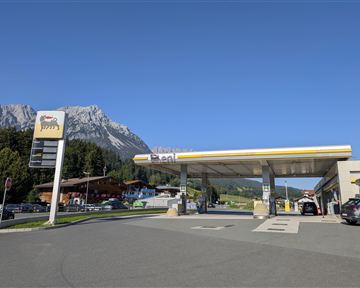 A gas station in front of a picturesque mountain landscape. The sky is clear and blue.