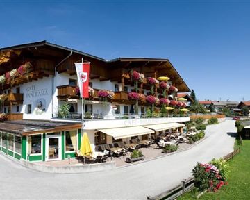 A cozy hotel in alpine style with balconies adorned with flower boxes. Surrounded by a picturesque landscape and lots of greenery.
