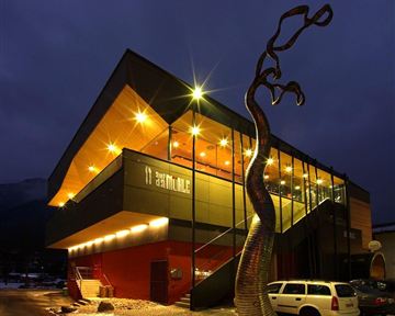 Ein modernes Gebäude mit spektakulärem Design bei Nacht. Vor der Fassade steht eine auffällige Skulptur.