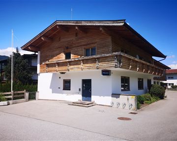 A modern building with a wooden facade and a balcony. It is situated in a quiet environment with a clear blue sky.
