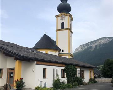 Eine bunte Kirche mit einem hohen Turm und einer markanten Kuppel. Im Hintergrund sind beeindruckende Berge zu sehen.